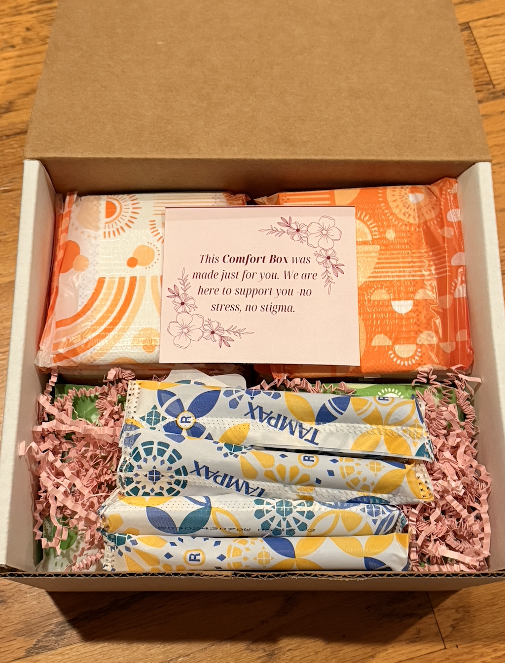 A Pads for Peers Comfort Box with menstrual products and a supportive note